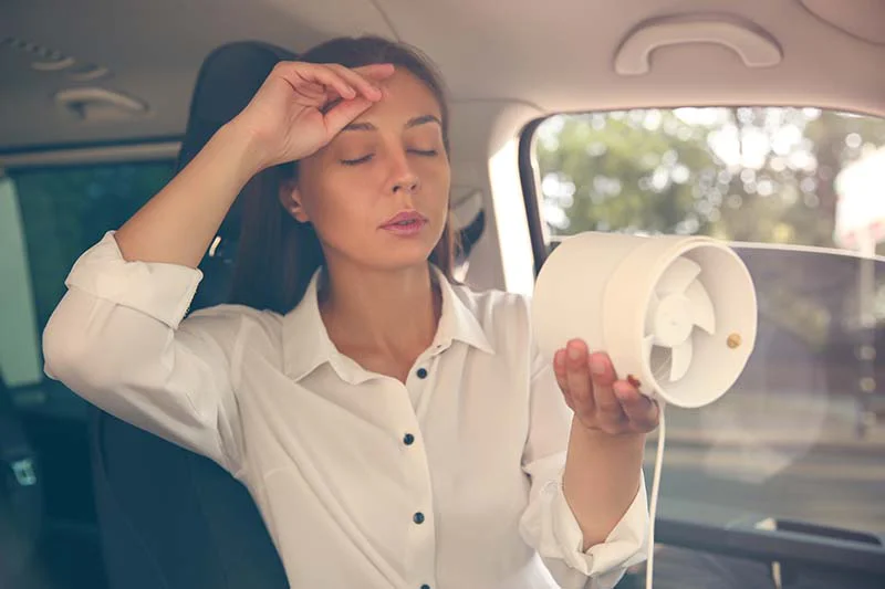 ac-3 Woman wiping brow while holding fan in front of her